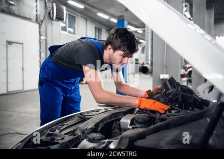 A mechanic is fixing a car engine. He is dressed in overalls and gloves Stock Photo