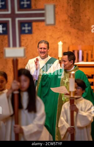 A robed deacon and an Asian American priest celebrate mass at the altar of a Southern California Catholic church. Stock Photo