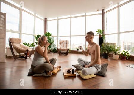 Young restful man and woman sitting on pillows and having tea on the floor Stock Photo