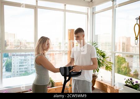 Young yoga trainer in activewear putting special equipment on female wrists Stock Photo