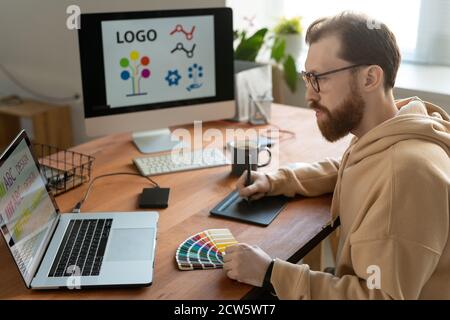 Young creative male freelance designer using tablet, stylus, laptop and palette Stock Photo