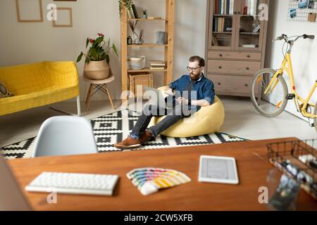 Young male designer sitting in comfortable armchair in front of his workplace Stock Photo