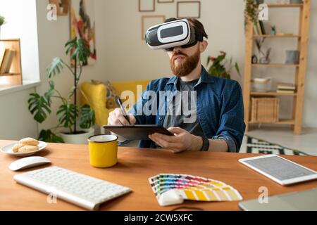 Young contemporary creative designer in vr headset drawing on tablet with stylus Stock Photo