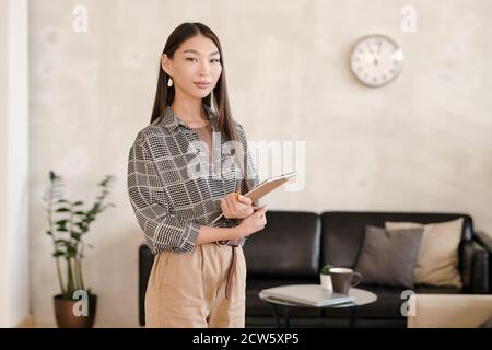Young serious pretty mixed-race businesswoman with notebook and pencil Stock Photo