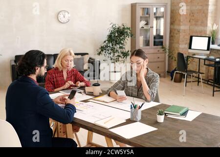 Three intercultural mobile application developers scrolling in smartphones Stock Photo
