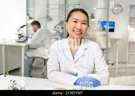 Young successful Asian female researcher in whitecoat and gloves looking at you Stock Photo