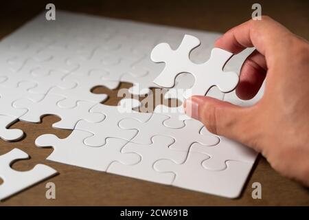 A white jigsaw puzzle on the table and a hand holding the pieces. Stock Photo
