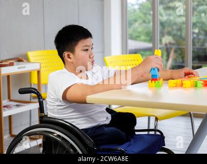 Disabled boy on wheelchair play colorful puzzle toy in classroom. Concept disabled child learning in school. Stock Photo