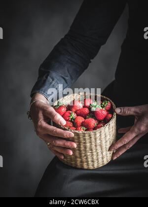 Woman's hands holding the basket full of strawberry. Low key photography. Stock Photo