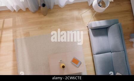 Cozy Living Room with Modern Interior, Grey Sofa, Tabel with a Book on it, and Wooden Flooring Lit By Warm Light out of the Window. Top View Camera Stock Photo