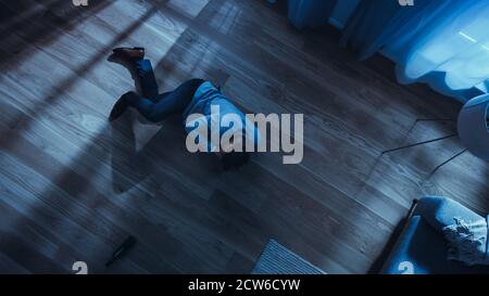 Poor Depressed Drunk Young Man is Crawling Towards a Sofa in an Apartment with Wooden Flooring. Dramatic Top View Camera Shot. Stock Photo