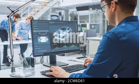 Over the Shoulder Shot of Engineer Working with CAD Software on Desktop Computer, Screen Shows Technical Drafts and Drawings. In the Background Stock Photo