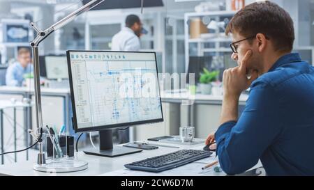 Over the Shoulder Shot of Engineer Working with CAD Software on Desktop Computer, Screen Shows Technical Drafts and Drawings. In the Background Stock Photo