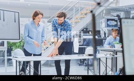 In the Industrial Engineering Facility: Young Female Designer Works with Chief Industrial Engineer, They have Discussion, Analyse and Correct Engine Stock Photo