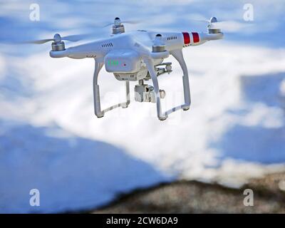 Quad-copter Drone with Video camera attached on search and rescue mission, flying low over snowy ground. Stock Photo