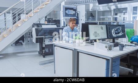 Senior Male Engineer Working on Design for Industrial Engine Prototype. Specialists Work with Drawings, Use Computers in Bright Engineering Facility Stock Photo