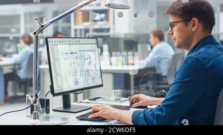 Over the Shoulder Shot of Engineer Working with CAD Software on Desktop Computer, Screen Shows Technical Drafts and Drawings. In the Background Stock Photo
