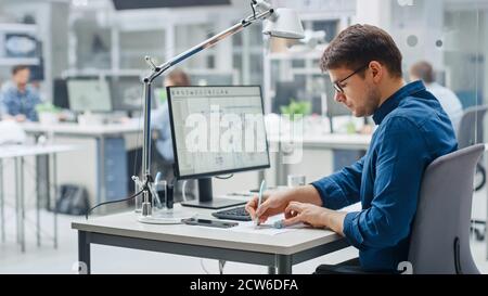 Over the Shoulder Shot of Engineer Working with CAD Software on Desktop Computer, Screen Shows Technical Drafts and Drawings. In the Background Stock Photo