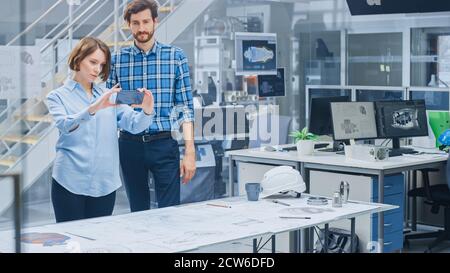 In the Industrial Engineering Facility: Female Designer with Chief Engineer Uses Smartphone for Augmented Reality App to Manipulate Engine Design Stock Photo