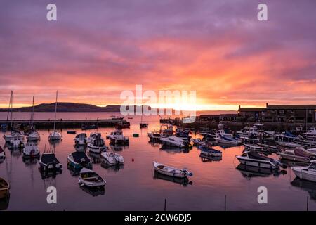 Lyme Regis, Dorset, UK. 28th Sep, 2020. UK Weather: The sky glows with autumn colour as the sun rises over the Cobb, Lyme Regis on a chilly September morning. Credit: Celia McMahon/Alamy Live News Stock Photo