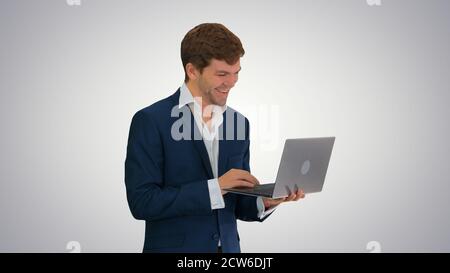 Smiling young businessman using laptop while standing on gradien Stock Photo