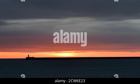 Newhaven Pier and Lighthouse, East Sussex as the sun sets behind the harbour arm Stock Photo