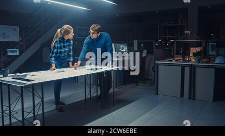 In the Dark Industrial Design Engineering Facility Male and Female Engineers Work on a Blueprints and Technical Drawings Using Conference Table Stock Photo