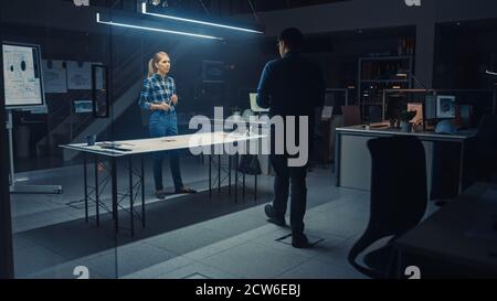 In the Dark Industrial Design Engineering Facility Male and Female Engineers Work on a Blueprints and Technical Drawings Using Conference Table. In Stock Photo