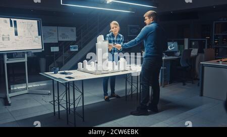 Late at Night in Architectural Agency, Team of Architects and Engineers Working on a City District Buildings Model Prototype. They Talk, Use Digital Stock Photo