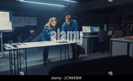 Industrial Design Engineering Facility Male and Female Engineers Work on a Blueprints and Technical Drawings Using Conference Table. Facility is Full Stock Photo