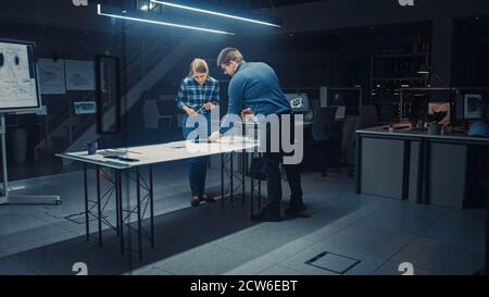 In the Dark Industrial Design Engineering Facility Male and Female Engineers Work on a Blueprints and Technical Drawings Using Conference Table. In Stock Photo