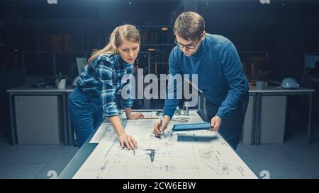 In the Dark Industrial Design Engineering Facility Male and Female Engineers Talk and Work on a Blueprints Using Conference Table. On the Desktop Stock Photo
