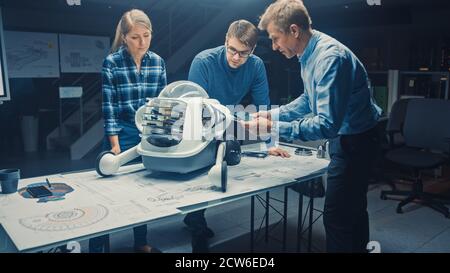 Robotics Engineering Facility Three Technical Engineers Talk and Work on a Wheeled Robot Prototype. In the Background High Tech Research Center with Stock Photo