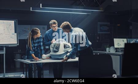 Late at Night in Robotics Engineering Facility Three Technical Engineers Talk and Work on a Wheeled Robot Prototype. In the Background High Tech Stock Photo