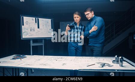 Two Young Software Development Engineers Talk and Use Smartphone with Augmented Reality for Reading and Interacting with Car and Engine Concept Stock Photo