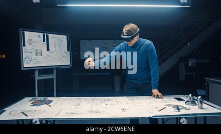 Software Development Engineer Wearing Virtual Reality Headset Gestures and Manipulates Components in Augmented Reality. Engineering Facility Has Desk Stock Photo