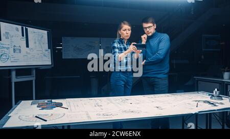 Two Young Software Development Engineers Talk and Use Smartphone with Augmented Reality for Reading and Interacting with Car and Engine Concept Stock Photo