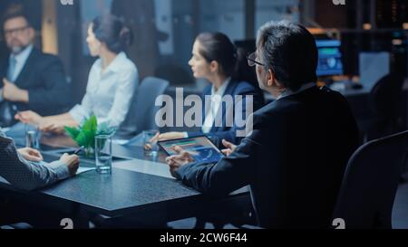 Late at Night In the Corporate Office Meeting Room: Executive Director Leads Hard Negotiations with Businesspeople. Over the Shoulder Back Shot Stock Photo