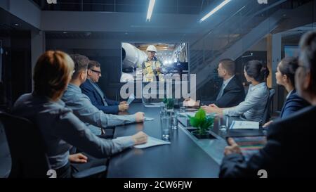 Late at Night In Corporate Meeting Room: Executives and Businesspeople Sitting at Negotiations Table Having Video Conference Call with Professional Stock Photo