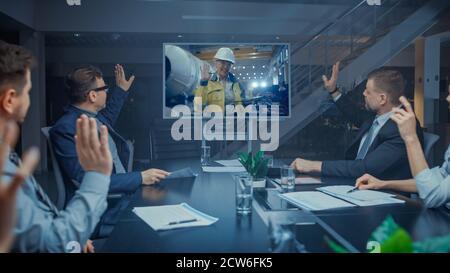 Late at Night In Corporate Meeting Room: Executives and Businesspeople Sitting at Negotiations Table Having Video Conference Call with Professional Stock Photo