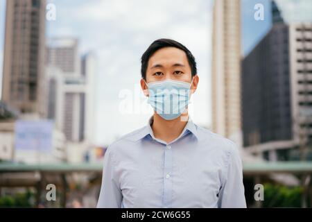 Asian businessman wearing protective Covid face covering facing camera, urban setting, city life, pandemic Stock Photo