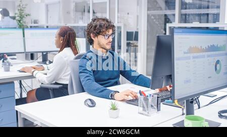 In the Big Busy Corporate Office Professional Worker Using Desktop Computer, Around Him Businesspeople and Experts Working with Clients, Having Stock Photo