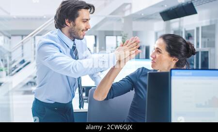 Two Professional Office Workers Work on Desktop Computer, Together Find Solution to a Problem and Cheerfully Celebrate Success by Doing High Five Stock Photo