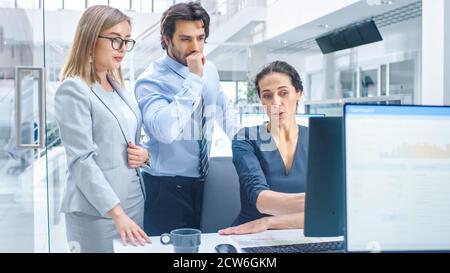 In Bright Modern Office: Office Worker Sitting and Working at Her Desktop Computer, Discusses Problem Solution with Her Project Manager and Team Stock Photo
