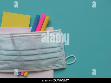 Face mask on top of coloring pens and notebook. Blue background. Copy space. Stock Photo