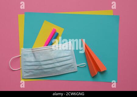 Face mask on top of coloring pens and papers with paper plane. Pink background. Stock Photo