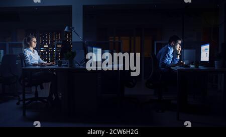 Working Late at Night in the Office: Businesspeople Use Desktop Computer, Analyzing, Using Documents, Solving Problems, Finishing Important Project Stock Photo