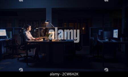 Working Late at Night in the Office: Businesswoman Uses Desktop Computer, Analyzing, Using Documents, Solving Problems, Finishing Important Project Stock Photo