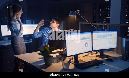 Late at Night in Modern Office: Office Worker Sitting and Working at His Desktop Computer, Discusses Problem Solution wit Project Manager, they Stock Photo