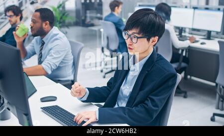 Young Professional Japanese Stock Broker Celebrates a Successful Deal. Diverse and Motivated Business People Work on Computers in Modern Open Office. Stock Photo